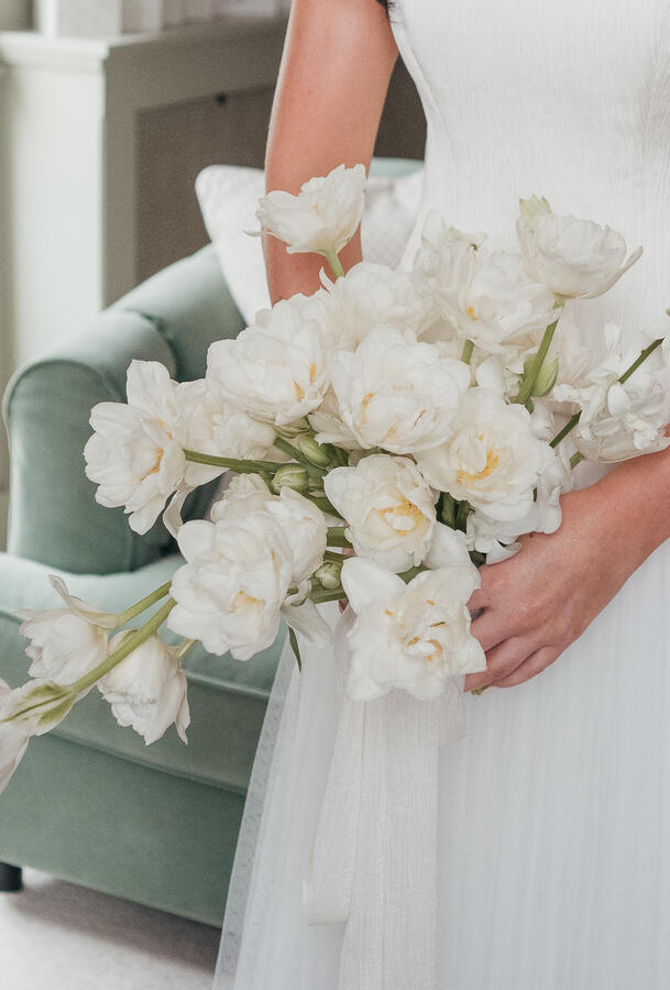 Close-up of a bride holding an elegant white wedding bouquet beside her dress.