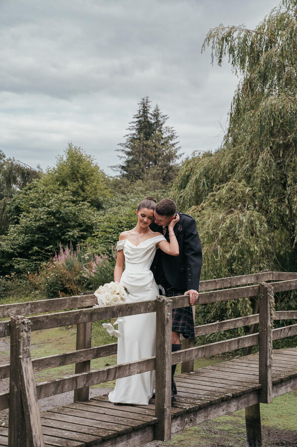 Newlyweds sharing a quiet romantic moment together on a wooden bridge after their ceremony.
